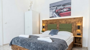 A bed with a grey blanket, a wooden headboard, and a painting of a car on the wall.