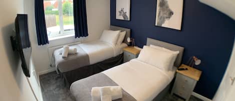 A hotel room with two single beds, a TV, a desk, and a window with curtains.