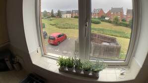 A room with a large window overlooking a residential area, a small window sill with potted plants, and a visible door. - The coach house views netflix sleeps 5 (Leicester)