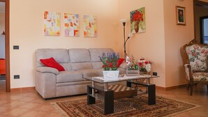 Un salón con sofá, mesa de centro, lámpara y sillón estampado. Hay tres cuadros en la pared y una alfombra en el suelo.