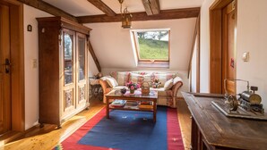 A cozy room with a wooden ceiling, a sofa with cushions, a coffee table, and a window with a view of a green landscape. - Apartment 'Achraintal 1' with Mountain View and Wi-Fi (Lindau)