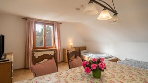 A bedroom with a bed, bedside table, lamp, window with curtains, and a table with a floral tablecloth and flowers. - Apartment 'Achraintal 1' with Mountain View and Wi-Fi (Lindau)