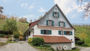 A traditional chalet with a steep roof, green shutters, and a gravel driveway. - Apartment 'Achraintal 1' with Mountain View and Wi-Fi (Lindau)