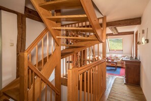 Un escalier en bois mène à une chambre située en mezzanine, qui offre une vue sur l’extérieur.
