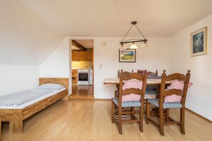 Une chambre avec un lit en bois, une table à manger avec des chaises, et une cuisine à l’arrière-plan.