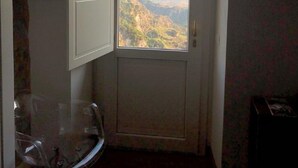 A room with a door leading to a balcony with a mountain view. There is a chair and a small table in the room.