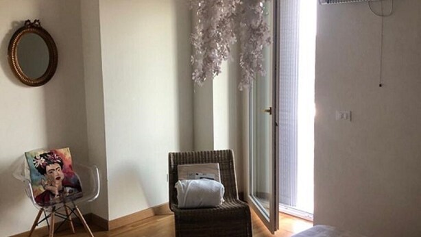 A bedroom with a bed, a chair, a painting, and a hanging light fixture.