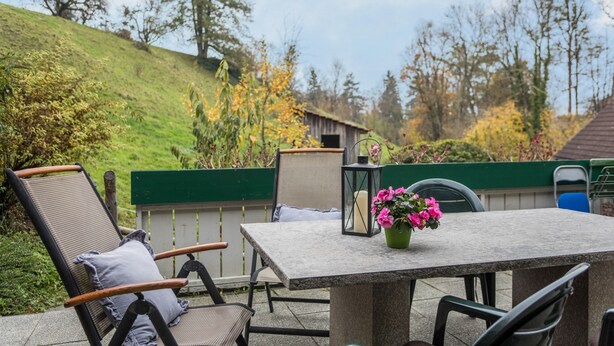 An outdoor patio with a table, chairs, and a flower vase.