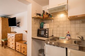 Une cuisine compacte équipée d’un four à micro-ondes, d’un grille-pain et d’une cuisinière. On y trouve un meuble en bois et un téléviseur fixé au mur.