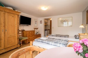 Une chambre à coucher avec une armoire en bois, une télévision, un lit avec une couette à carreaux, un bureau et une chaise.