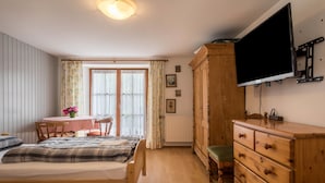 A bedroom with a bed, wooden dresser, television, and a window with curtains.