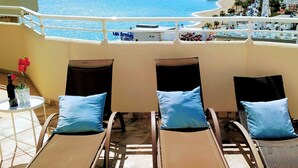 Un balcone con tre poltrone da relax, un tavolino con una bottiglia e fiori, e vista sulla spiaggia e sullo skyline della città.