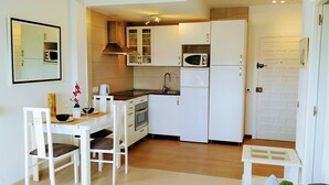 Una cucina compatta con mobili bianchi, un forno a microonde, un piano cottura e un lavello. È presente un tavolo da pranzo con sedie e un piccolo tavolino.