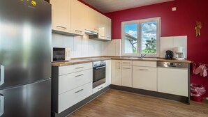 A modern kitchen with stainless steel appliances, white cabinetry, and a red accent wall. - Holiday Apartment "Buche" with Wi-Fi, Mountain View, Terrace & Garden (Neukirch)