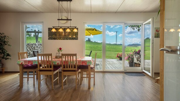 A dining area with a table, chairs, and a view through large glass doors. - Holiday Apartment "Buche" with Wi-Fi, Mountain View, Terrace & Garden (Neukirch)