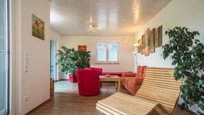 A modern living room with a wooden floor, red and orange furniture, and a large potted plant. - Holiday Apartment "Buche" with Wi-Fi, Mountain View, Terrace & Garden (Neukirch)