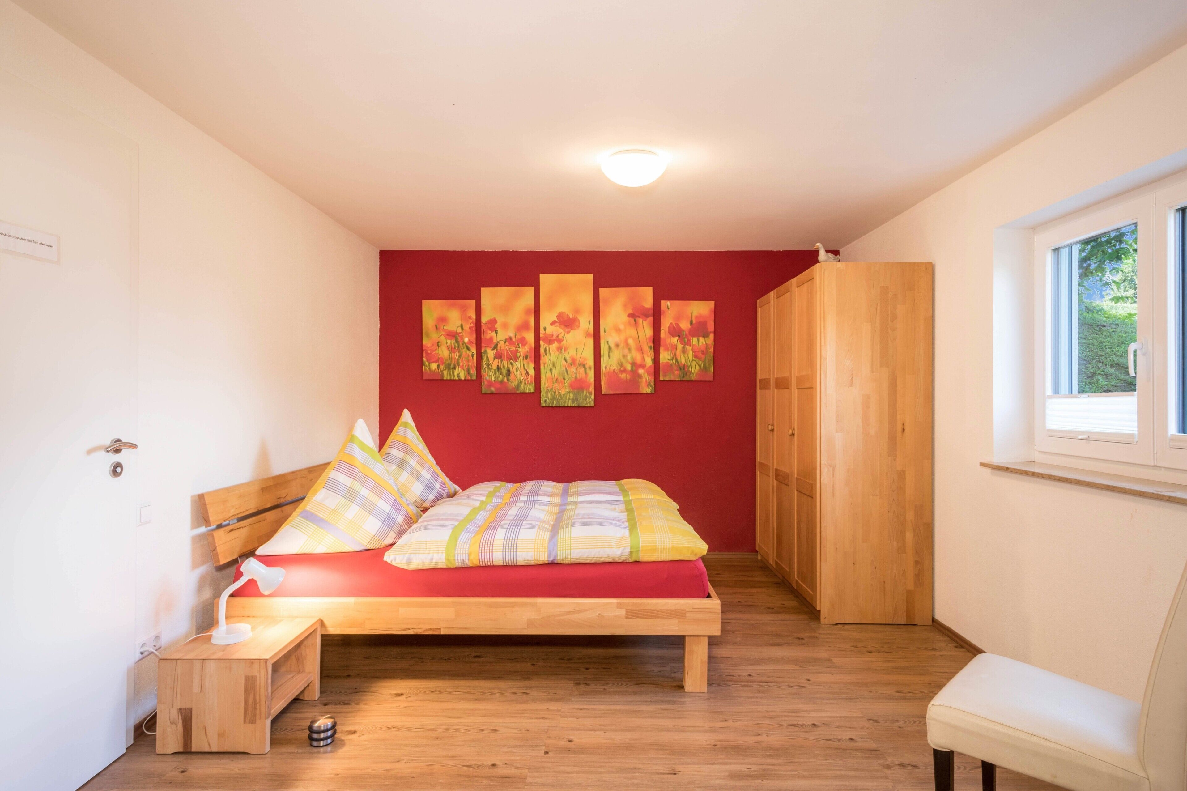 A bedroom with a wooden bed, a red wall, and a window.