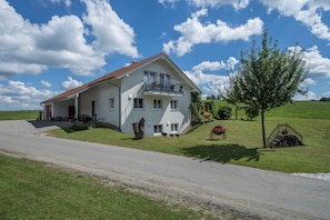 Ein zweistöckiges Haus mit Balkon, Auffahrt und einem Rasen mit Baum und Blumenbeet.