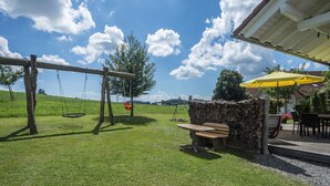 Un espace extérieur verdoyant avec une balançoire, un muret en pierre et un banc en bois.