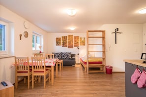 Ein gemütlicher Raum mit Holztisch, Stühlen, einer Couch, einem Etagenbett und einer kleinen Küche.