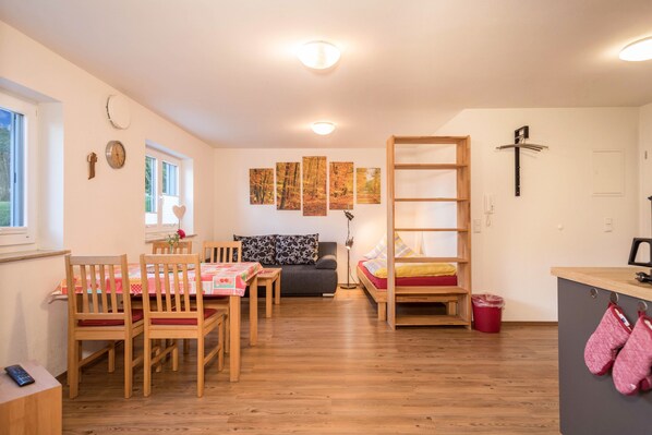 Ein gemütlicher Raum mit Holztisch, Stühlen, einer Couch, einem Etagenbett und einer kleinen Küche.