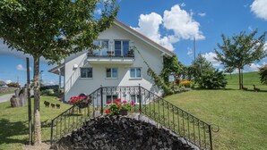 Une maison à deux étages avec un balcon, un mur en pierre et une cour gazonnée.