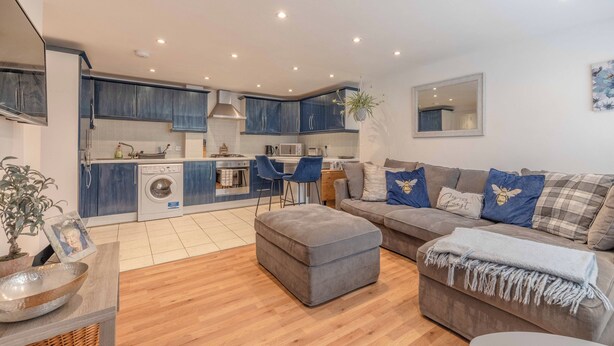 A modern kitchen with built-in appliances, a dining area with blue chairs, and a living room with a grey sofa and ottoman. - Windsor Town Centre Sleeps 6 (Windsor)