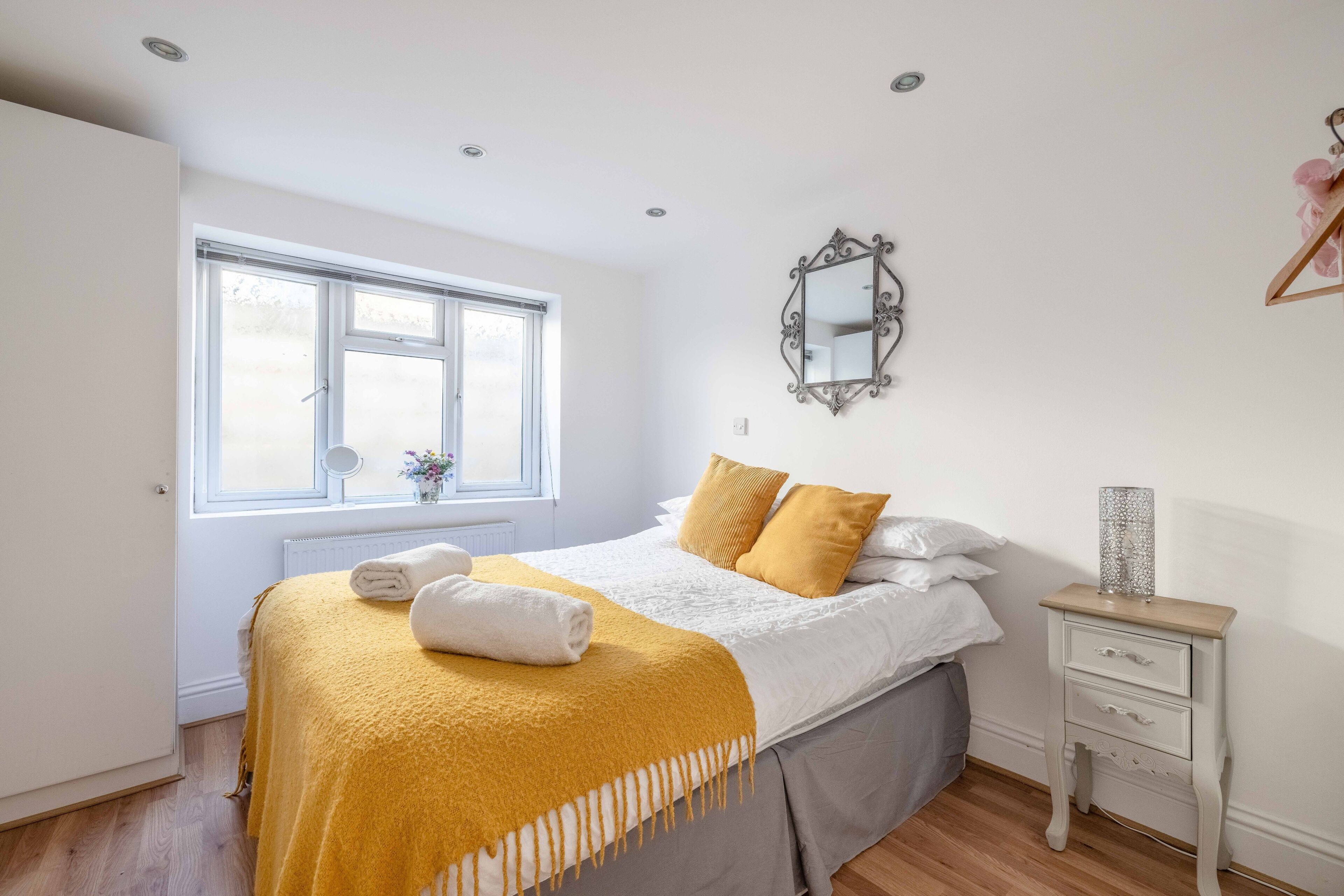 A bedroom with a bed, a bedside table, a mirror, and a window.