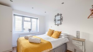 A bedroom with a bed, a bedside table, a mirror, and a window. - Windsor Town Centre Sleeps 6 (Windsor)
