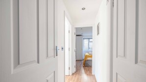 A narrow hallway with white doors leading to a room with a bed and a window. - Windsor Town Centre Sleeps 6 (Windsor)