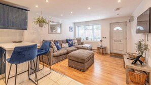 A modern living room with a sofa, ottoman, and bar stools. There is a kitchen area with a counter and cabinets. - Windsor Town Centre Sleeps 6 (Windsor)