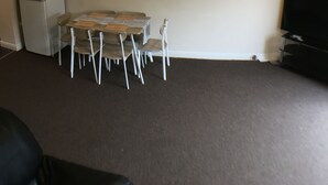 Ein Wohnzimmer mit Esstisch, Stühlen, einem Kühlschrank und gerahmten Bildern an der Wand.