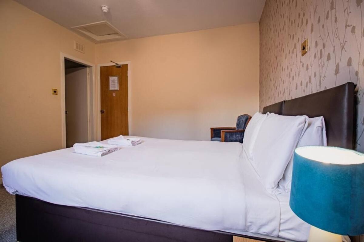 Una habitación de hotel con cama, mesita de noche, lámpara y puerta.
