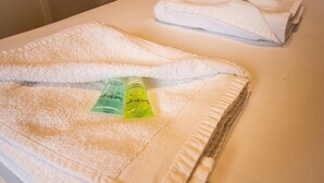 Een netjes gevouwen witte handdoek op een bed, met twee kleine groene verpakkingen erop.