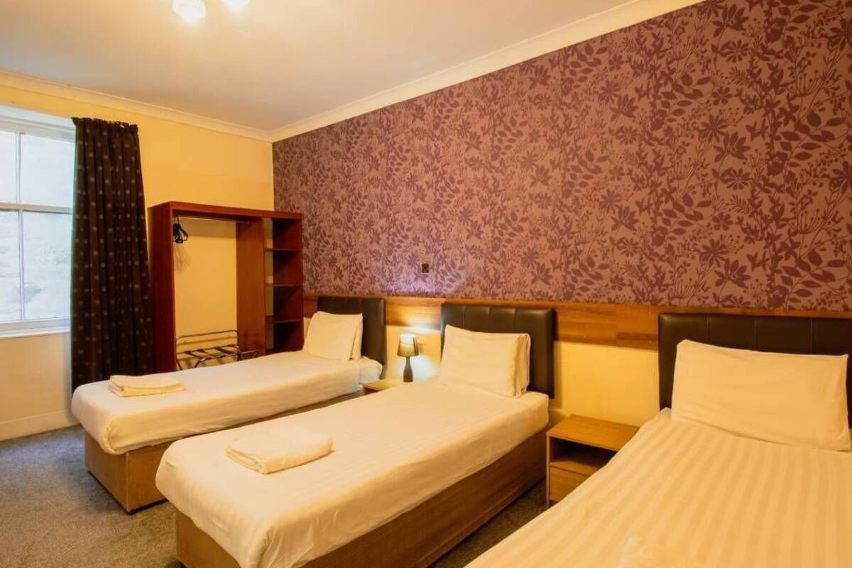 Habitación de hotel con dos camas individuales, un armario de madera, un espejo y un papel tapiz con estampado floral.