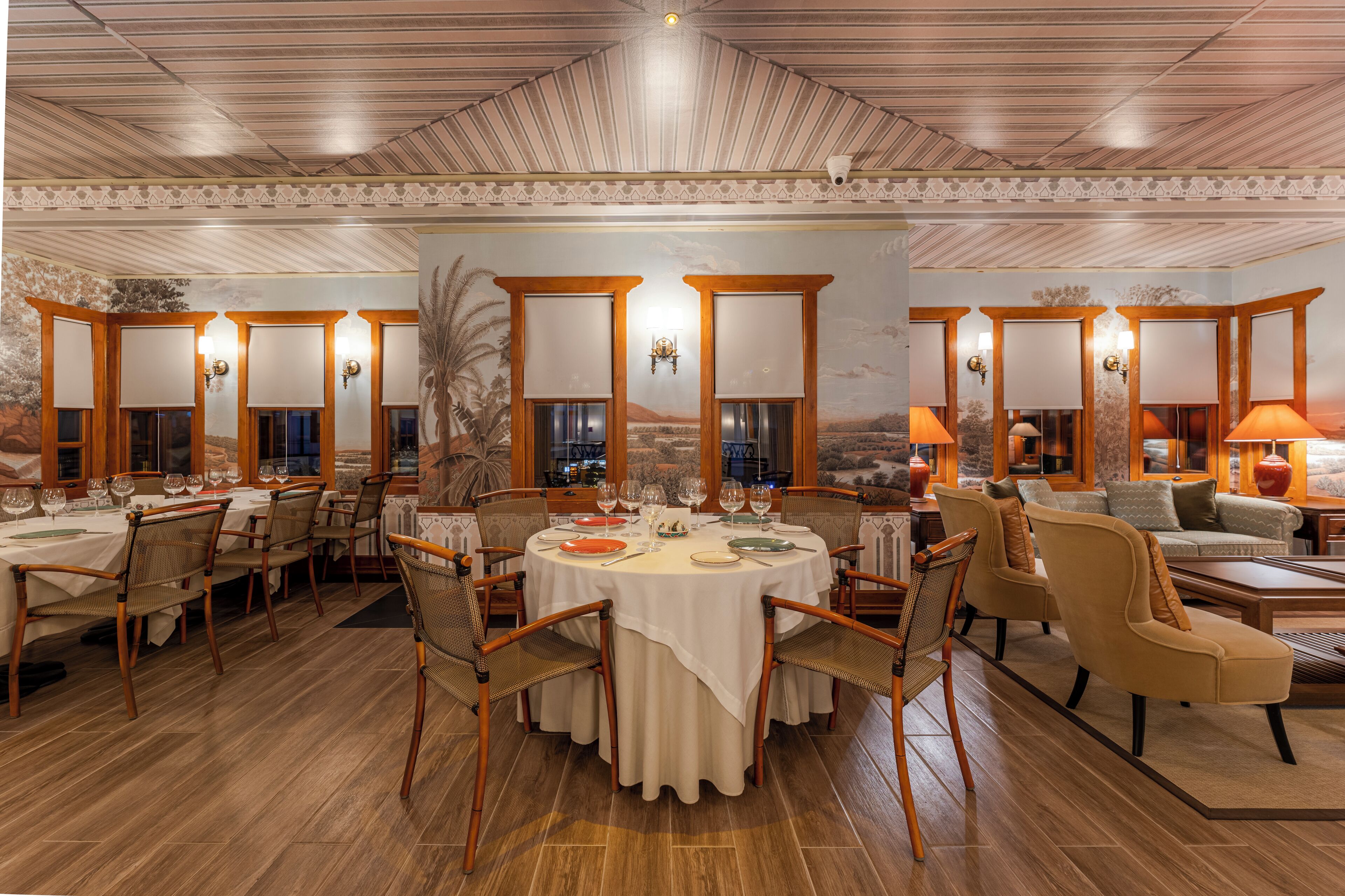 A spacious dining area with round tables, wooden chairs, and a mural on the wall.