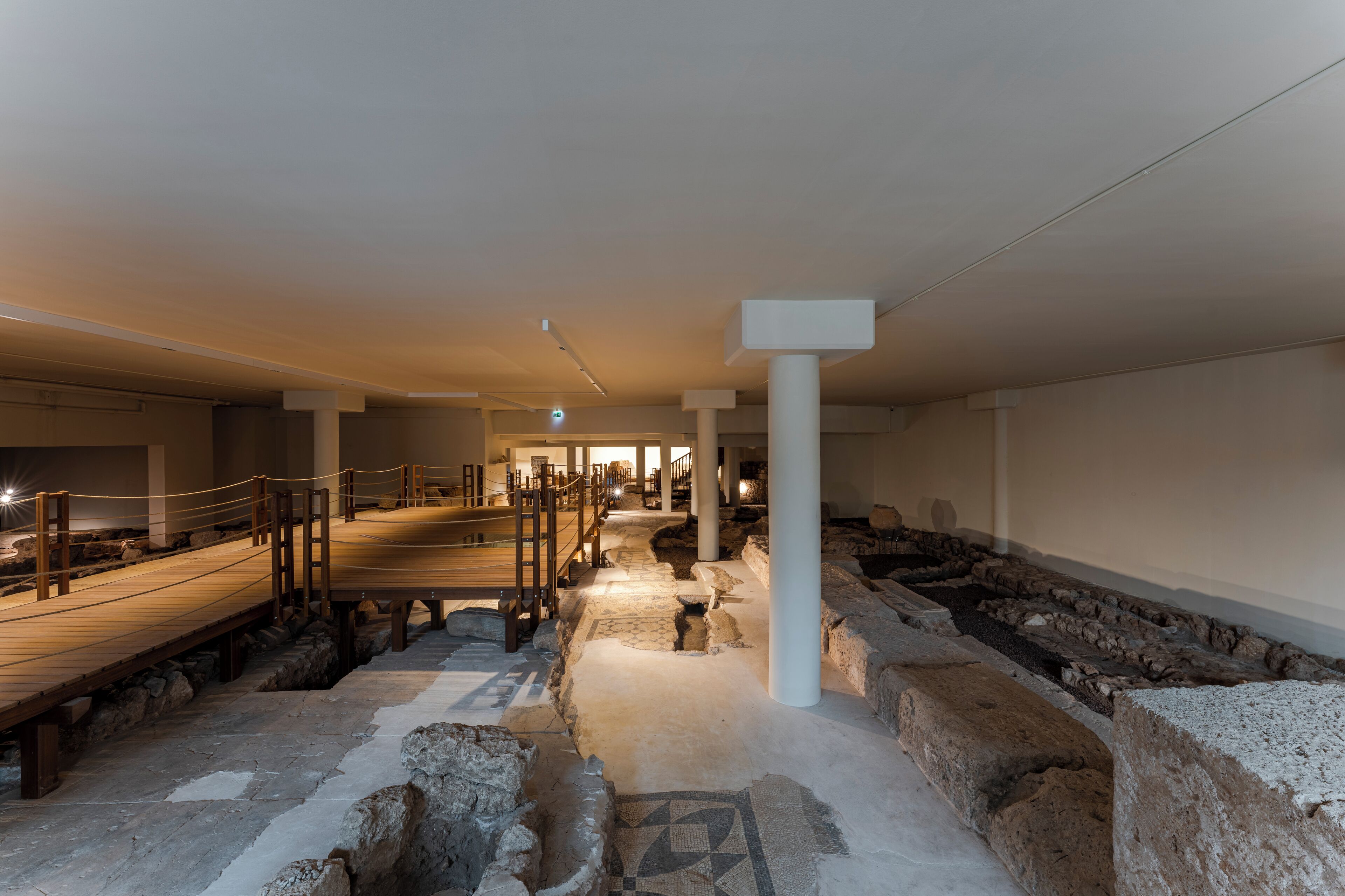 An ancient archaeological site with stone structures, a wooden walkway, and a central column.