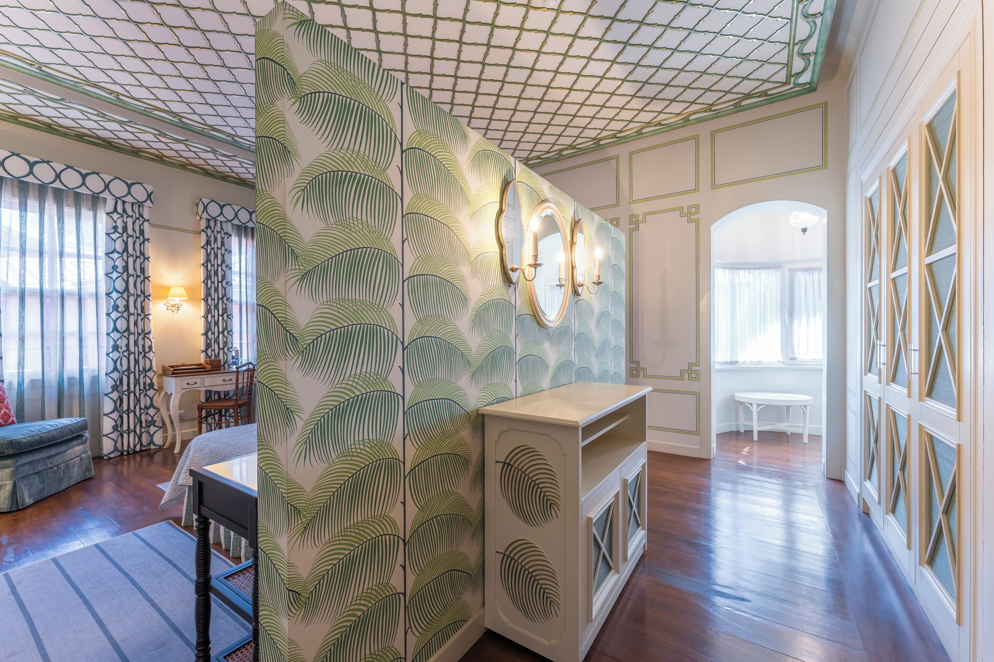 A room with a patterned wall, a wooden floor, a white table, and a bench.