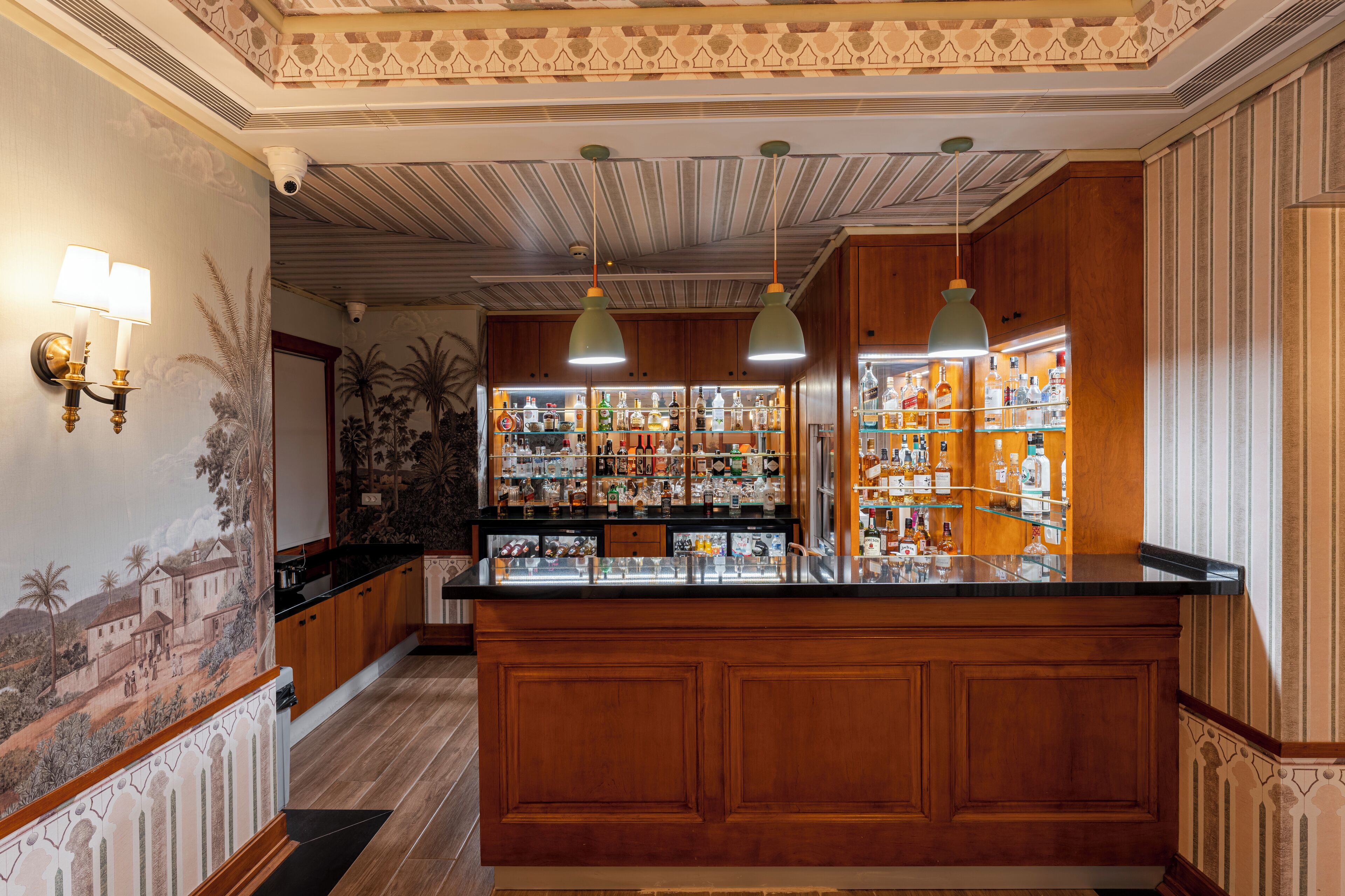 A bar area with wooden cabinets, hanging pendant lights, and a variety of bottles and glasses on shelves.