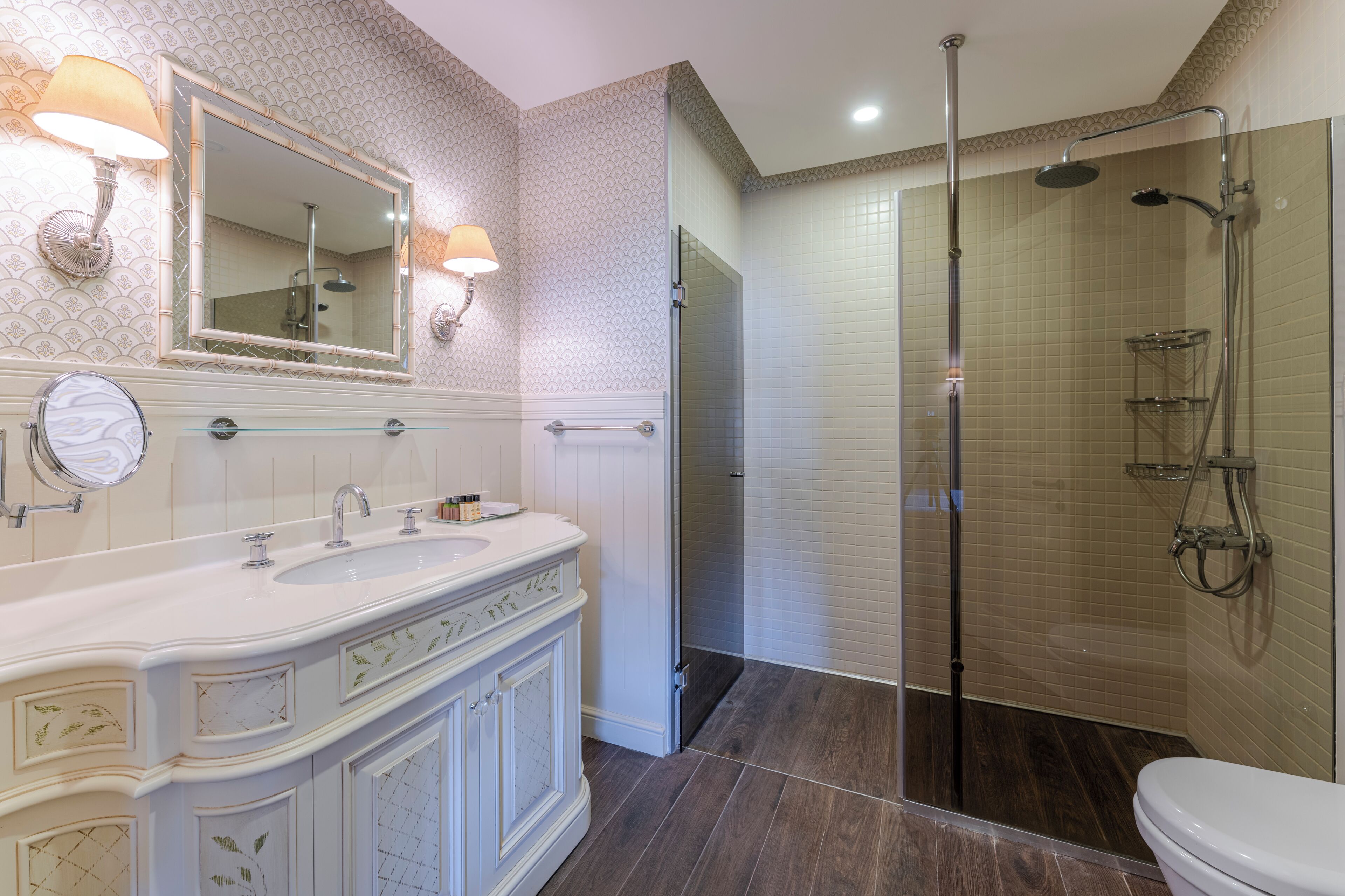A bathroom with a double sink vanity, a large mirror, a glass-enclosed shower, and a toilet.