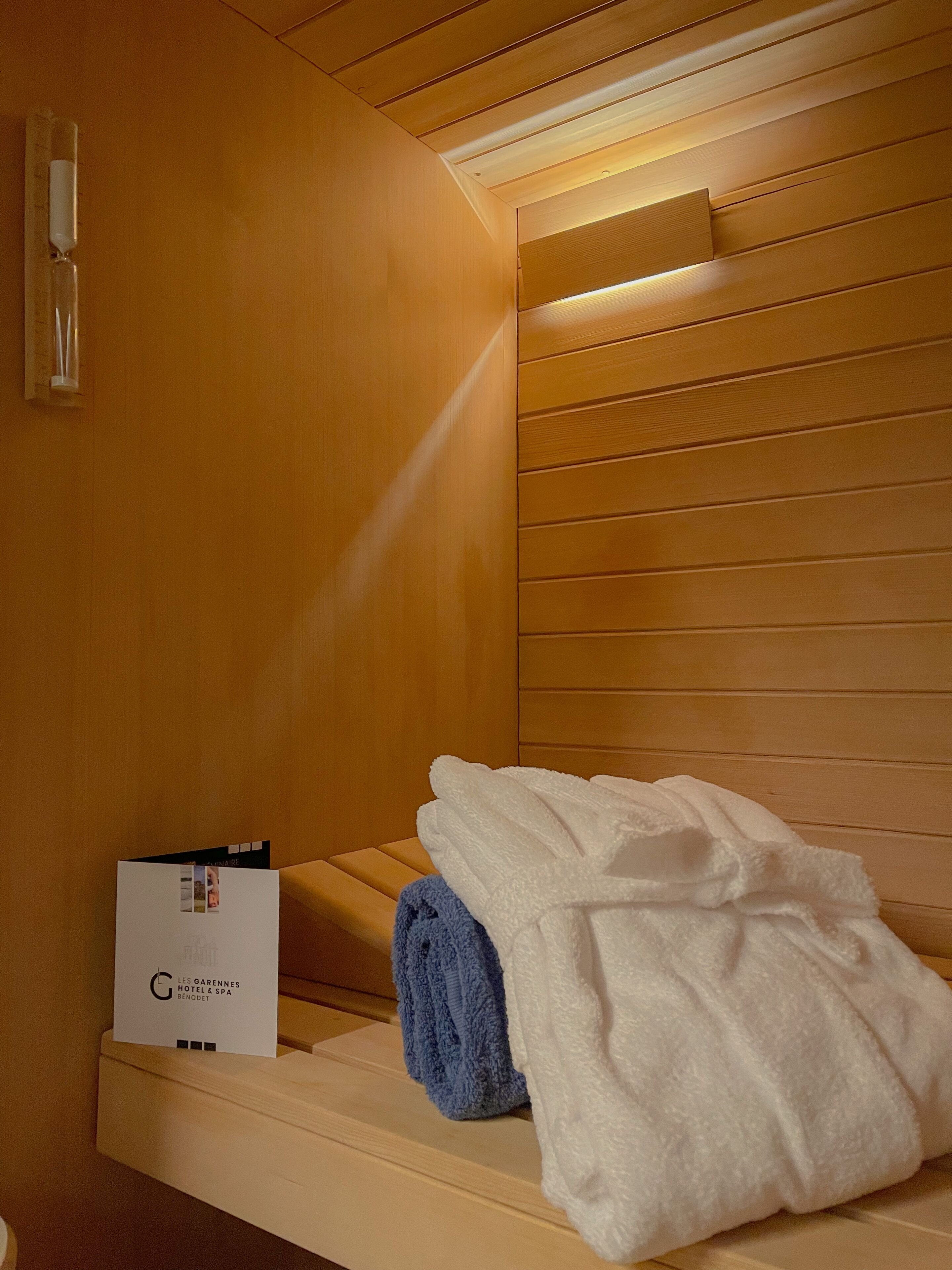 A sauna room with wooden paneling, a towel, and a brochure on a shelf.