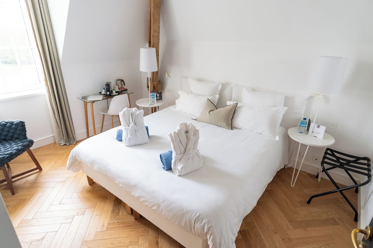 A hotel room with a large bed, a desk, a chair, and a lamp.