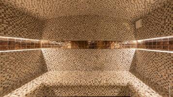 A bathroom with mosaic tile walls and floor, a bench, and a wall-mounted mirror.