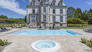 A large, elegant building with a swimming pool and hot tub in front.