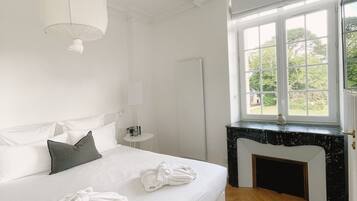 A bedroom with a large bed, a window with a view of greenery, a fireplace, and a hanging light fixture.
