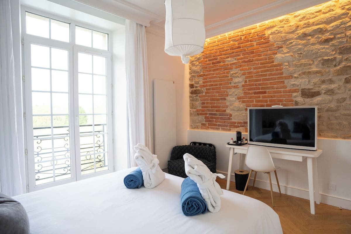A hotel room with a large bed, a TV, a desk, and a brick wall.