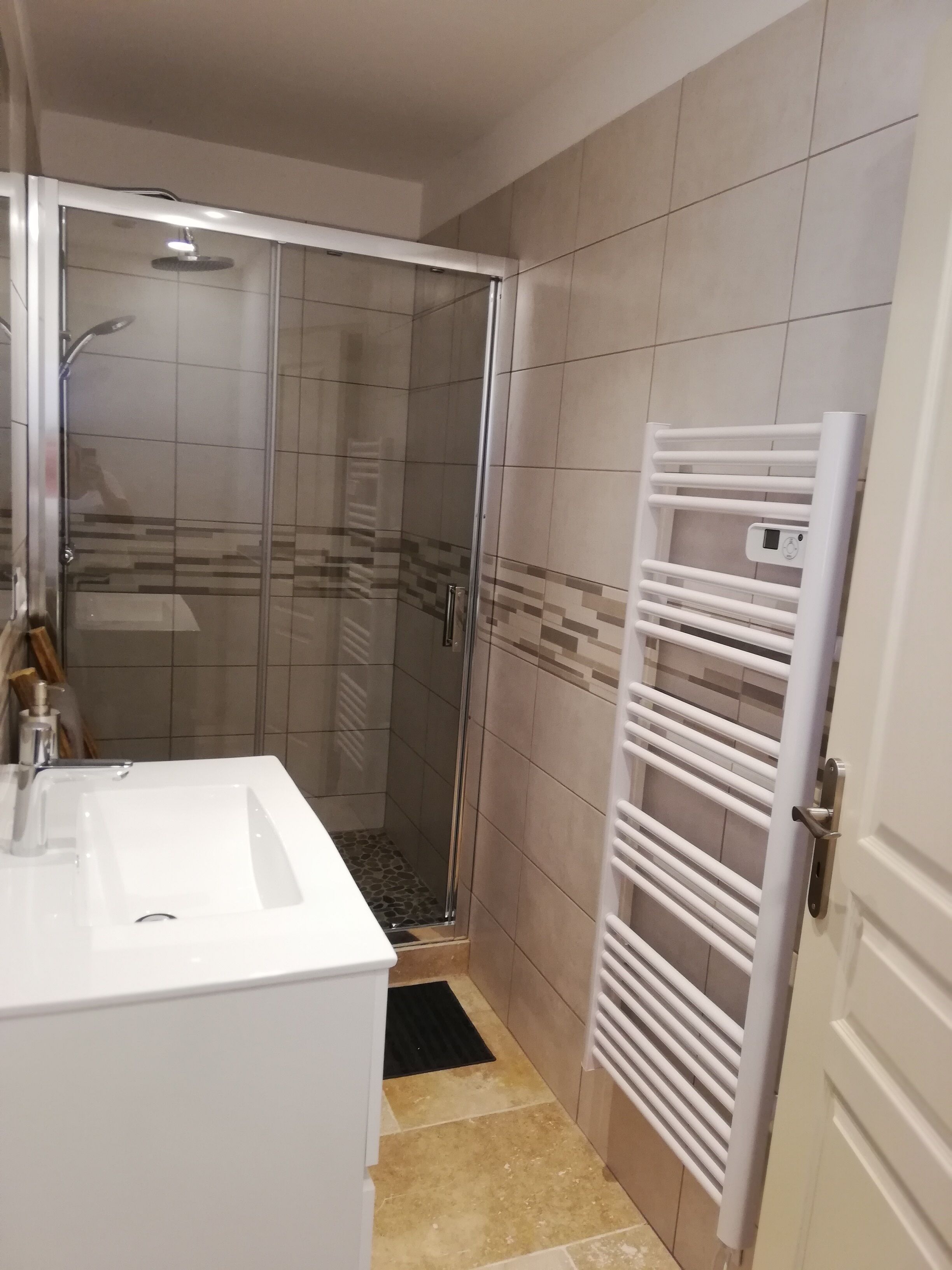Ein Badezimmer mit einer Duschkabine, einem weißen Waschbecken und einem Handtuchhalter.