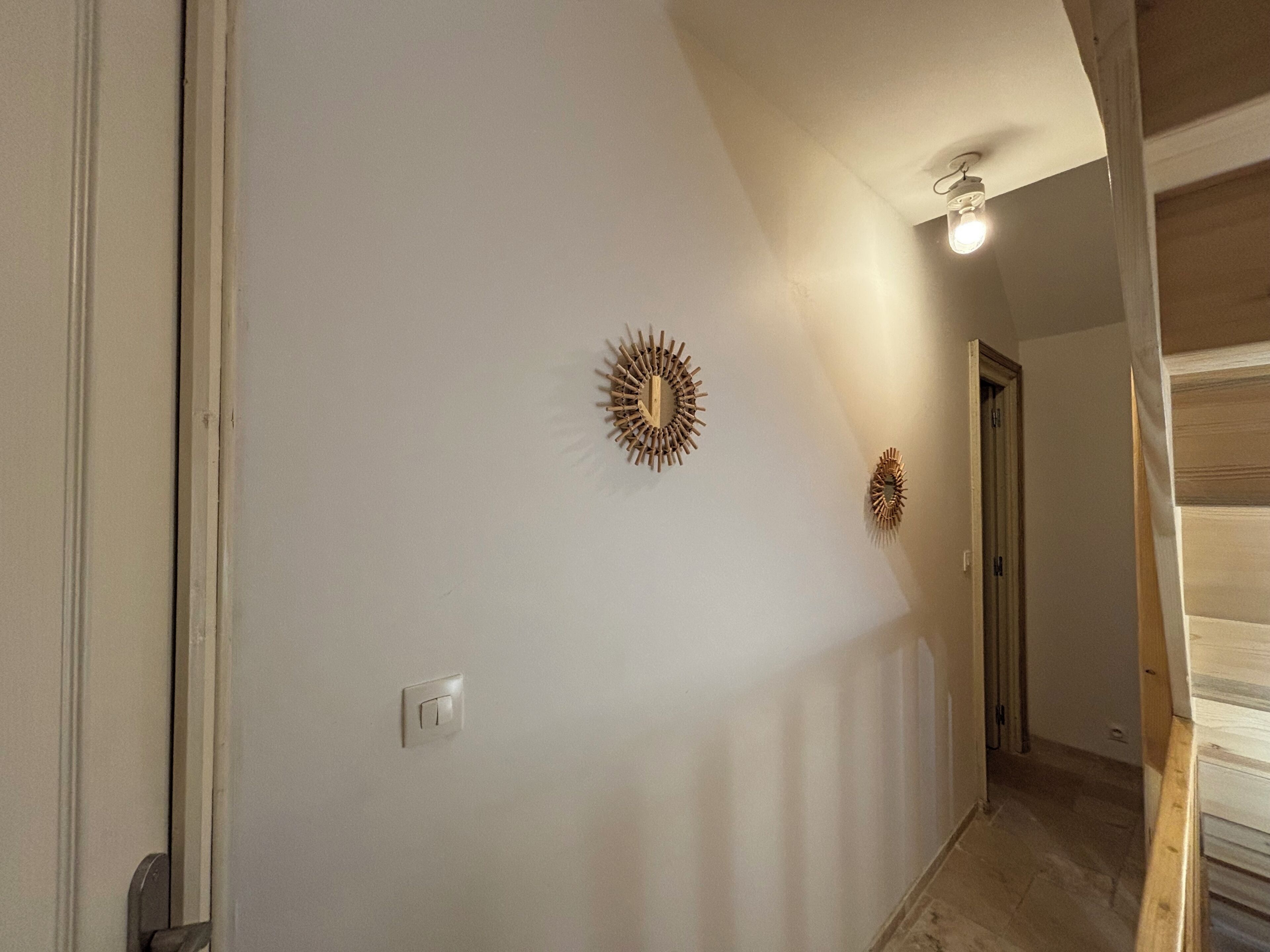 Ein Flur mit Lichtschalter, einer Tür und zwei Wanddekorationen im Sonnenstrahl-Design.