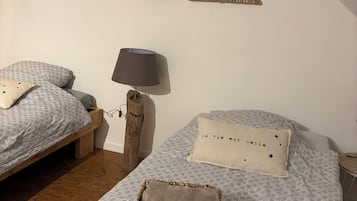 Une chambre avec deux lits, une décoration murale en forme de feuille, une lampe et un panier en osier posé sur l’un des lits.