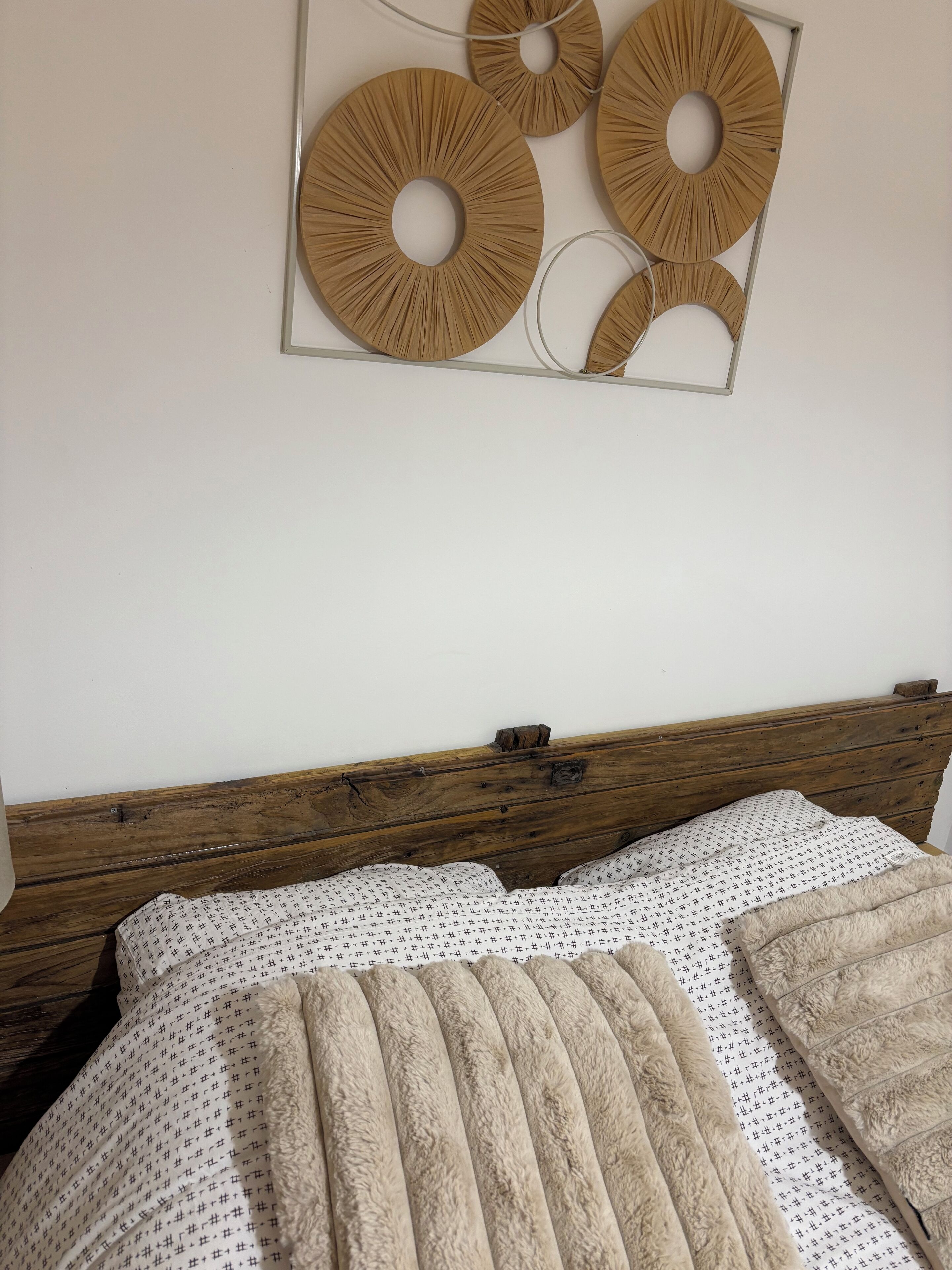 A bed with a wooden headboard, a patterned blanket, and a decorative wall piece.
